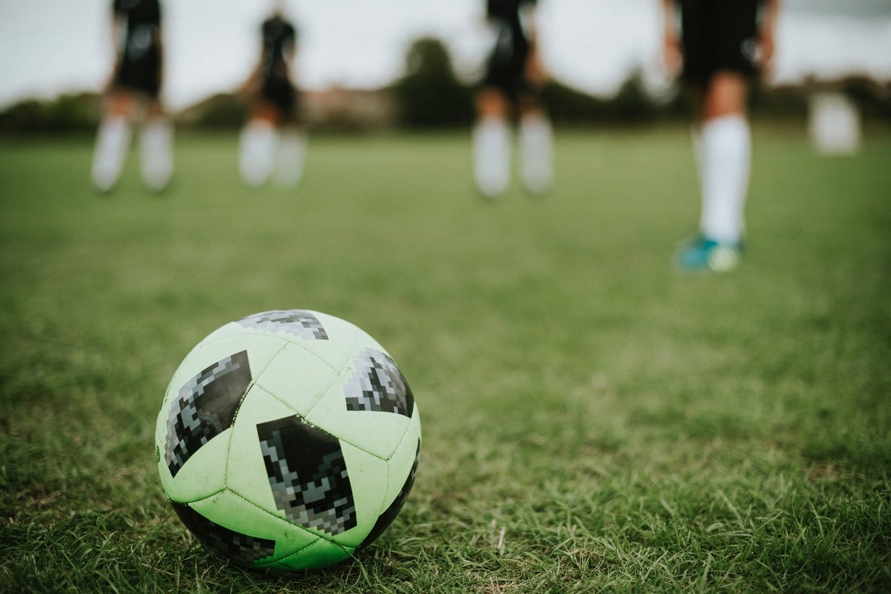 Soccer ball on soccer field with soccer players blurred in the background.
