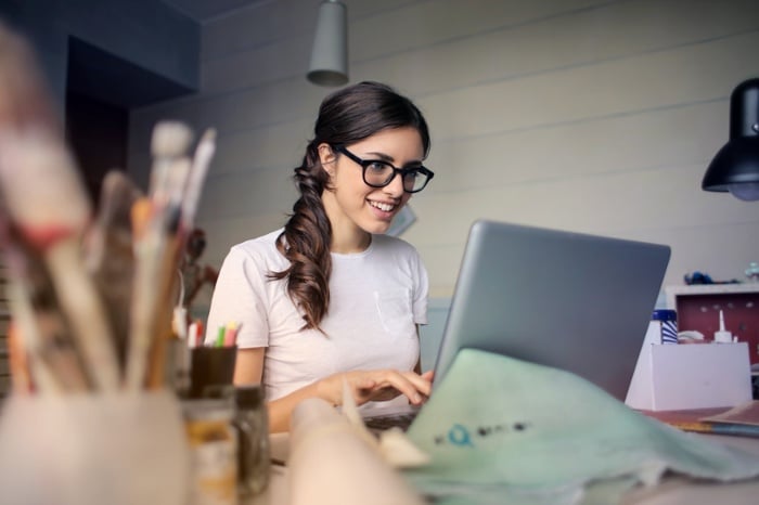 A girl with glasses sitting at her desk browsing on the computer. 